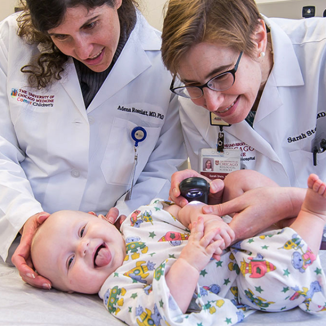 Two female physicians observing a laughing infant patient